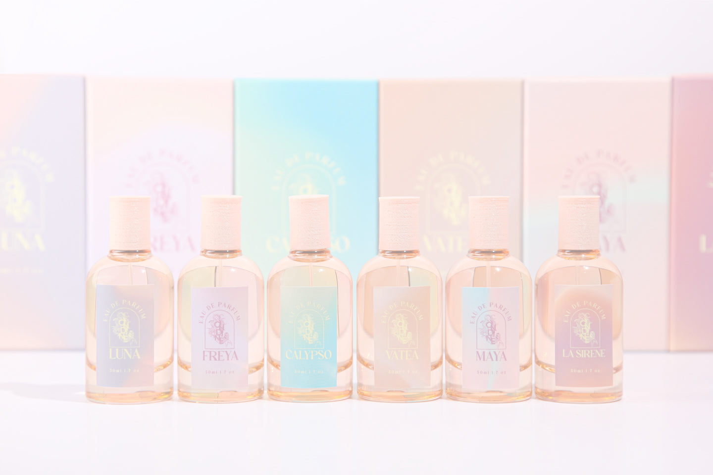 Ondine Perfume, six peachy pink coloured glass bottles with pastel gradient labels in various pastel colours, featuring pink coloured landfill biodegradable caps. Background shows matching pastel coloured gradient boxes for all 6 perfumes